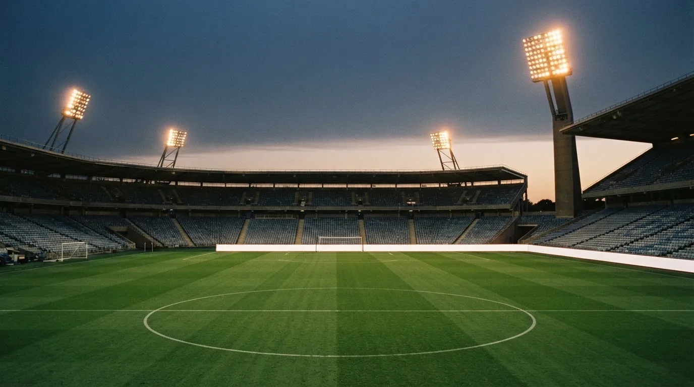 Een leeg voetbalstadion met lichtmasten bij schemering