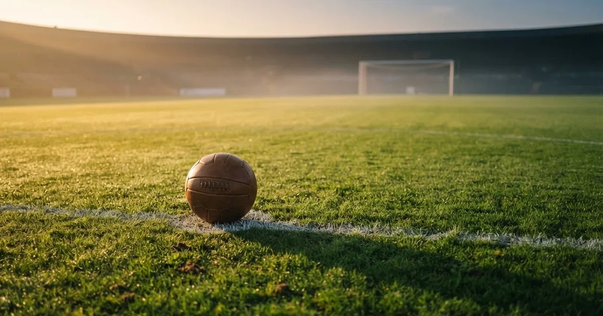 Een voetbal op de middenstip van een grasveld in het ochtendlicht
