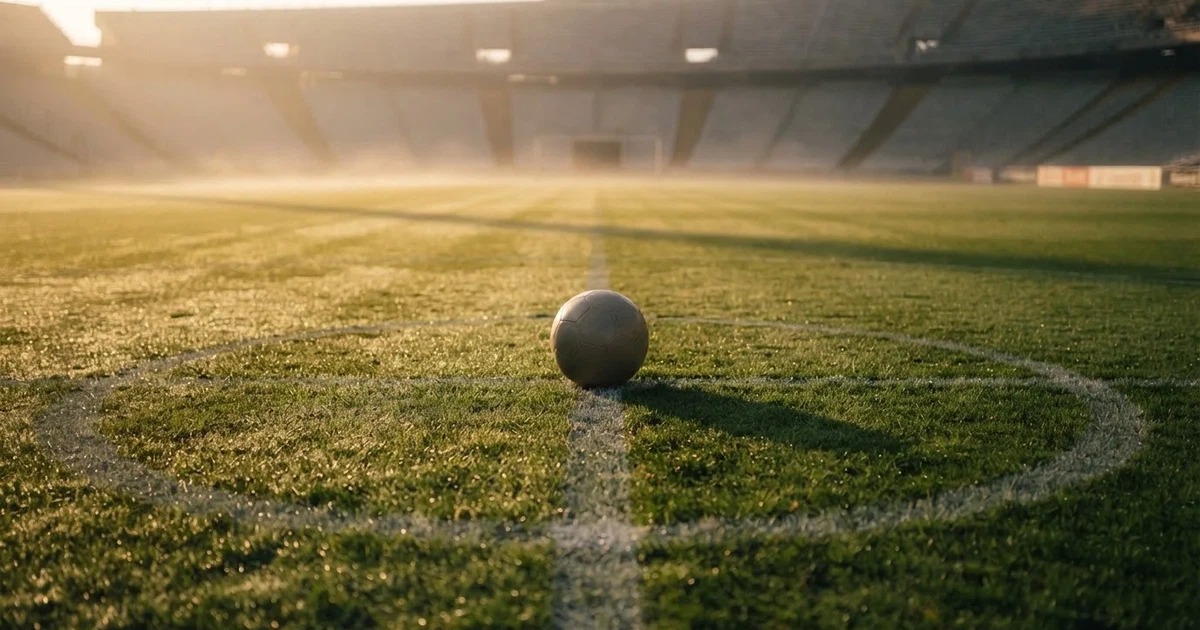Een voetbal op de middenstip van een grasveld in het ochtendlicht