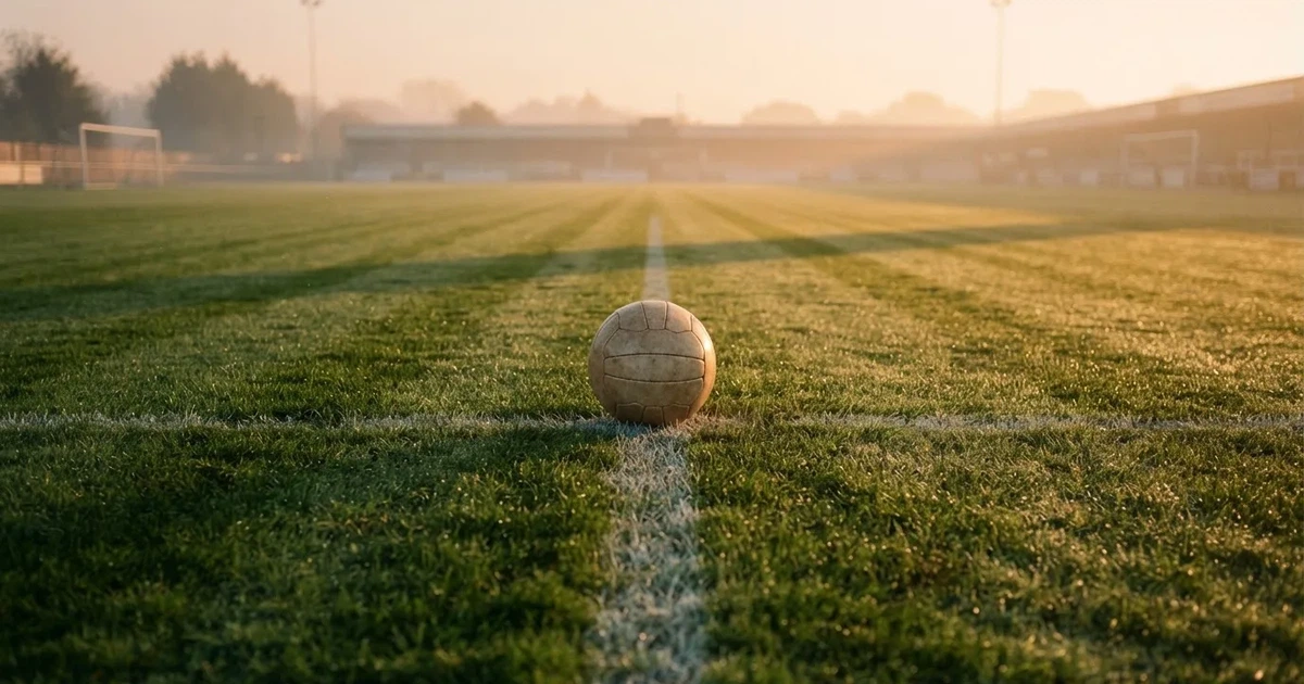 Een voetbal op de middenstip van een grasveld in het ochtendlicht