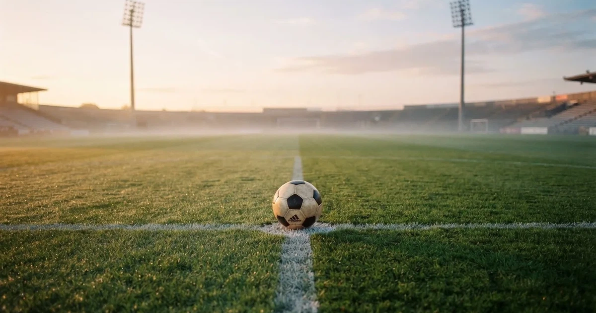 Een voetbal op de middenstip van een grasveld in het ochtendlicht