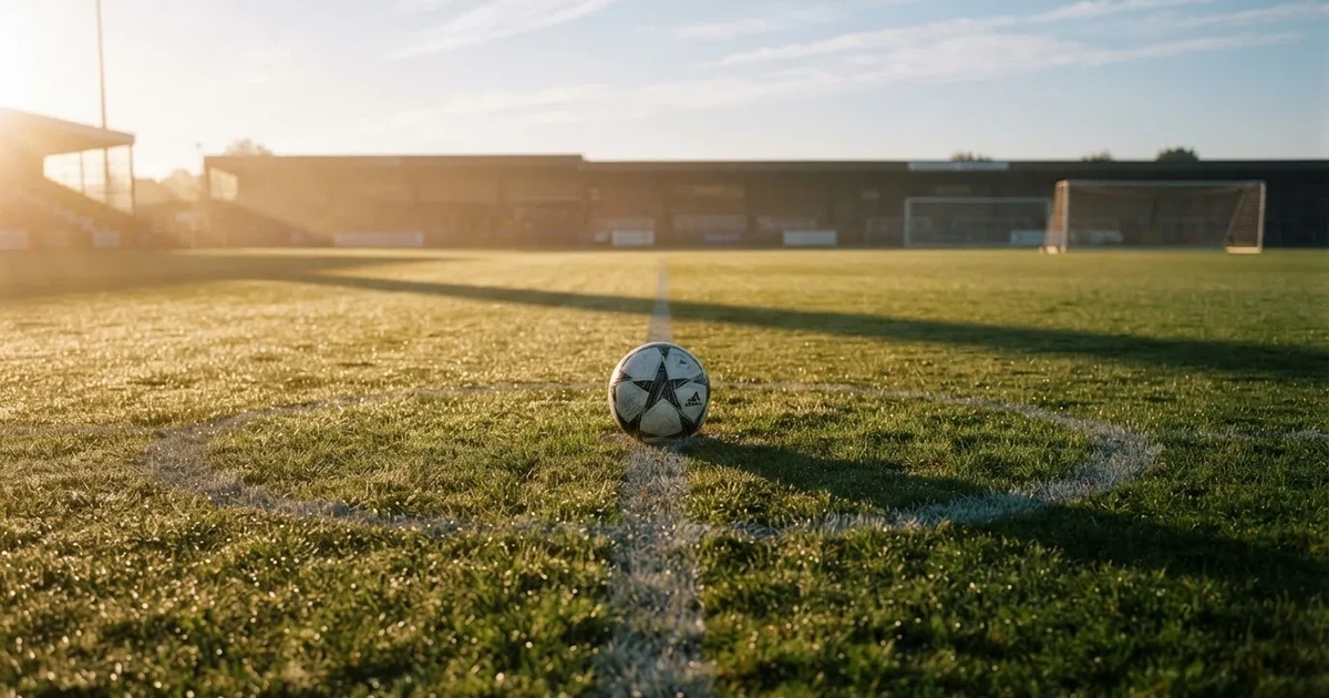 Een voetbal op de middenstip van een grasveld in het ochtendlicht