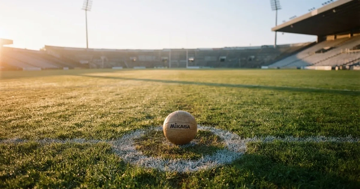 Een voetbal op de middenstip van een grasveld in het ochtendlicht