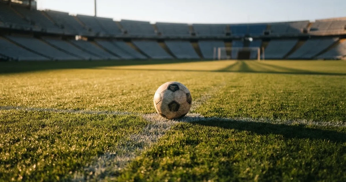 Een voetbal op de middenstip van een grasveld in het ochtendlicht